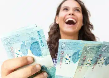 Mulher sorrindo segura notas de R$ 100 ao representar pagamento de R$ 1.486 ou mais para brasileiros com CPF de finais de 0 a 9.