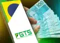 Celular exibindo logotipo do FGTS ao lado de mão segurando leque de notas de cem reais
