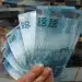 Mão segurando notas de R$ 100, representando os pagamentos de R$ 50 mil pelo governo em maio.