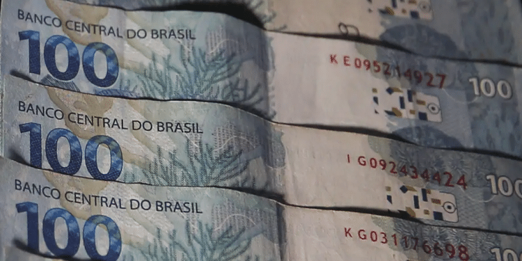 Quatro cédulas de R$ 100 do Banco Central do Brasil empilhadas, mostrando números de série e elementos de segurança, simbolizando o pagamento do INSS de 1º a 5 de junho.