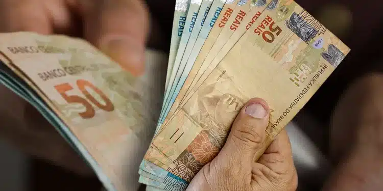 Mãos segurando notas de R$ 50 que representam o teto do INSS pago a aposentados em maio.