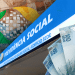 Placa da Previdência Social com logo do INSS e notas de 100 e 50 reais em composição gráfica, simbolizando o teto do INSS 2026.