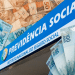 Fachada azul do INSS com logo oficial rodeada por notas de 50 e 100 reais brasileiros espalhadas, simbolizando os pagamentos do INSS no mês de maio.