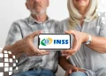 Casal de idosos segurando celular com logotipo do INSS em destaque na tela