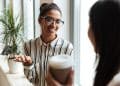 Duas mulheres conversando de forma amigável em ambiente de trabalho durante pausa para café.