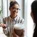 Duas mulheres conversando de forma amigável em ambiente de trabalho durante pausa para café.