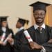 Jovem formando de beca e capelo sorri segurando o diploma