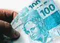 Mão segura cédulas de R$ 100, em cena que ilustra o pagamento da primeira parcela da renegociação no Novo Desenrola Brasil