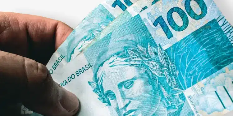 Mão segura cédulas de R$ 100, em cena que ilustra o pagamento da primeira parcela da renegociação no Novo Desenrola Brasil