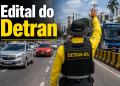 Agente do DETRAN-BA com colete amarelo e chapéu de fiscalização ergue a mão para orientar veículos em avenida de Salvador