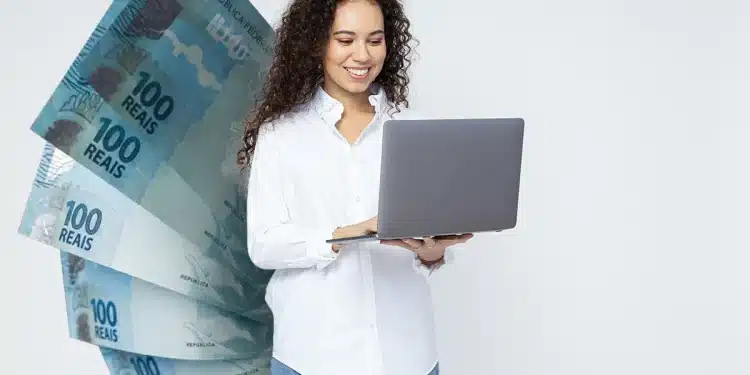 Jovem de cabelos cacheados segura laptop cinza enquanto sorri, com notas de 100 reais em composição ao lado.