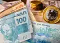 Cédulas de R$ 100 e moedas de real em destaque, em referência aos cinco cargos que pagam R$ 100 mil por mês no Brasil em 2026, segundo o Guia Salarial.