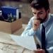 Homem preocupado analisando documento após perda de emprego em escritório.