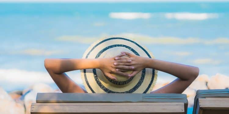 Pessoa relaxa em espreguiçadeira diante do mar, em imagem que ilustra planejamento de folgas e feriadões em 2026.