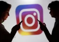 Silhuetas de uma mulher e um homem usando smartphones em frente ao logotipo colorido do Instagram, representação dos recursos de segurança ampliados pela Meta para usuários menores de idade.
