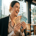 Mulher de blazer preto e blusa bege ri segurando leque de notas de 50 e 100 reais em restaurante urbano, simbolizando as opções de renda extra para quem trabalha um turno.