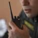 Vigilante de uniforme preto com inscrição amarela segura rádio comunicador próximo à boca durante ronda, simbolizando as opções de renda extra para vigilantes.