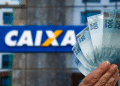 Mão segurando quatro notas de R$ 100 em frente ao logotipo da Caixa Econômica Federal, simbolizando o saque de até R$ 6.220 liberado nesta quarta, 27/5, para mais brasileiros.