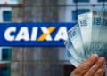 Mão segura cédulas de cem reais diante de fachada da Caixa Econômica Federal, em referência ao saque de até R$ 6.220
