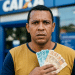 Homem segura notas de real junto ao peito e, ao redor, a fachada azul de uma agência da Caixa