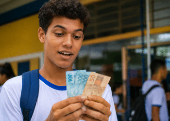 Estudante de uniforme conta cédulas de real em frente a uma escola