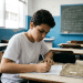 Jovem estudante do ensino médio escreve em caderno pautado dentro da sala de aula enquanto treina temas de redação para o Enem 2026