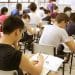 Sala de aula com diversos estudantes sentados em carteiras realizando uma prova com folhas e canetas