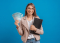 Jovem sorridente segurando notas de 100 reais e prancheta preta.