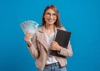 Jovem sorridente segurando notas de 100 reais e prancheta preta.