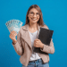Jovem sorridente segurando notas de 100 reais e prancheta preta.