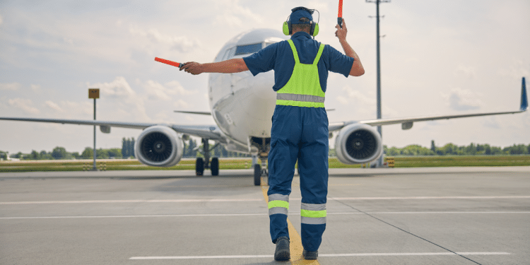 Profissional guia avião comercial no pátio de aeroporto durante operação.