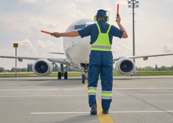 Profissional guia avião comercial no pátio de aeroporto durante operação.