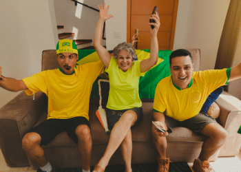Torcedores vibram assistindo jogo do Brasil com bandeira e camisas amarelas.