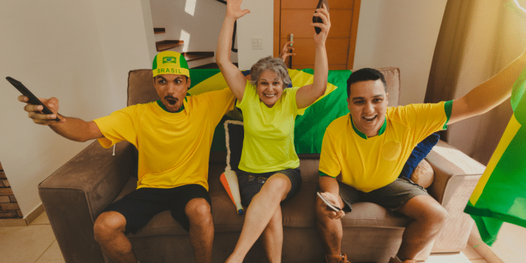 Torcedores vibram assistindo jogo do Brasil com bandeira e camisas amarelas.