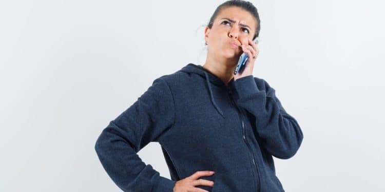 Mulher pensativa com expressão curiosa ao telefone em fundo claro.