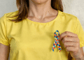 Mulher com camiseta amarela segurando laço de quebra-cabeça colorido, símbolo do autismo.