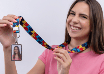 Jovem sorridente exibe crachá com cordão de peça de quebra-cabeça colorido.
