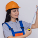 Profissional com trena e capacete laranja.