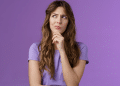 Mulher pensativa com expressão curiosa em fundo roxo.