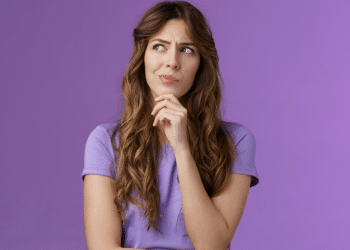 Mulher pensativa com expressão curiosa em fundo roxo.