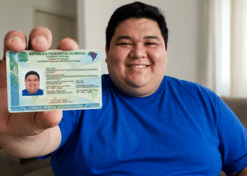 Homem sorridente exibe carteira de identidade brasileira em destaque.