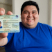 Homem sorridente exibe carteira de identidade brasileira em destaque.