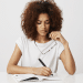 Jovem mulher refletindo enquanto escreve em caderno branco minimalista.