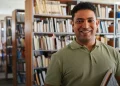 Homem segurando livros em biblioteca, representando estudante que pode ingressar em curso técnico com certificação do Encceja.