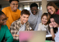 Jovens sorrindo e olhando juntos para um notebook em ambiente moderno.