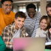 Jovens sorrindo e olhando juntos para um notebook em ambiente moderno.