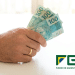Trabalhador segura notas de R$100 com logo do FGTS ao lado.