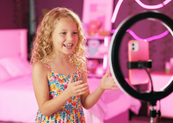 Criança gravando vídeo em quarto decorado com luzes neon para redes sociais.