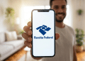 Homem exibe aplicativo da Receita Federal em celular com ambiente doméstico moderno.