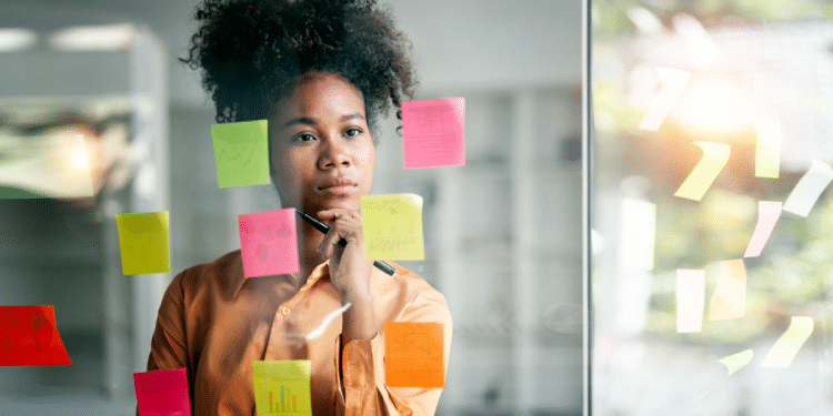 Jovem analisa ideias em mural de post-its coloridos no escritório.